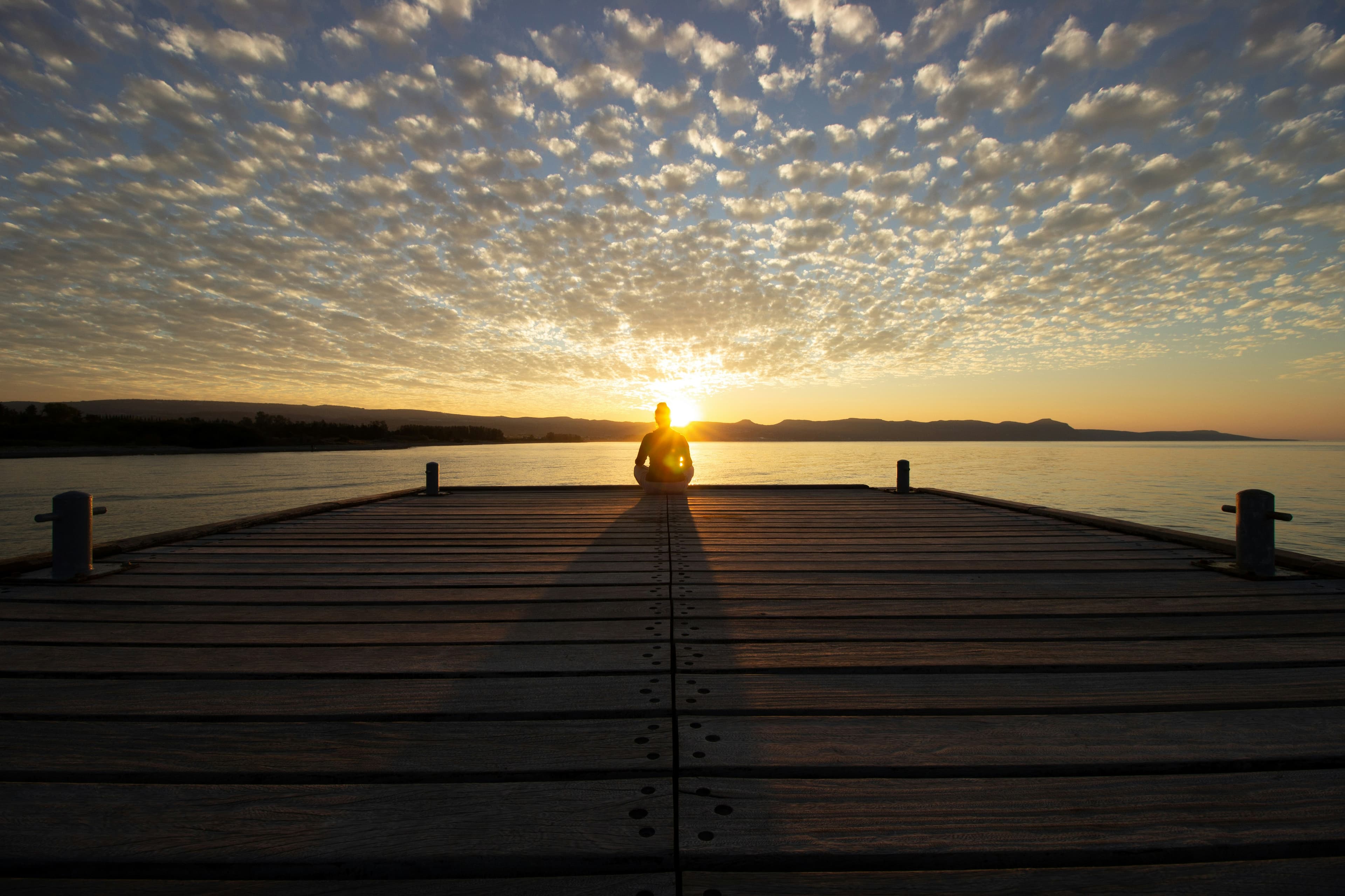 Person meditating peacefully on wooden dock at sunset